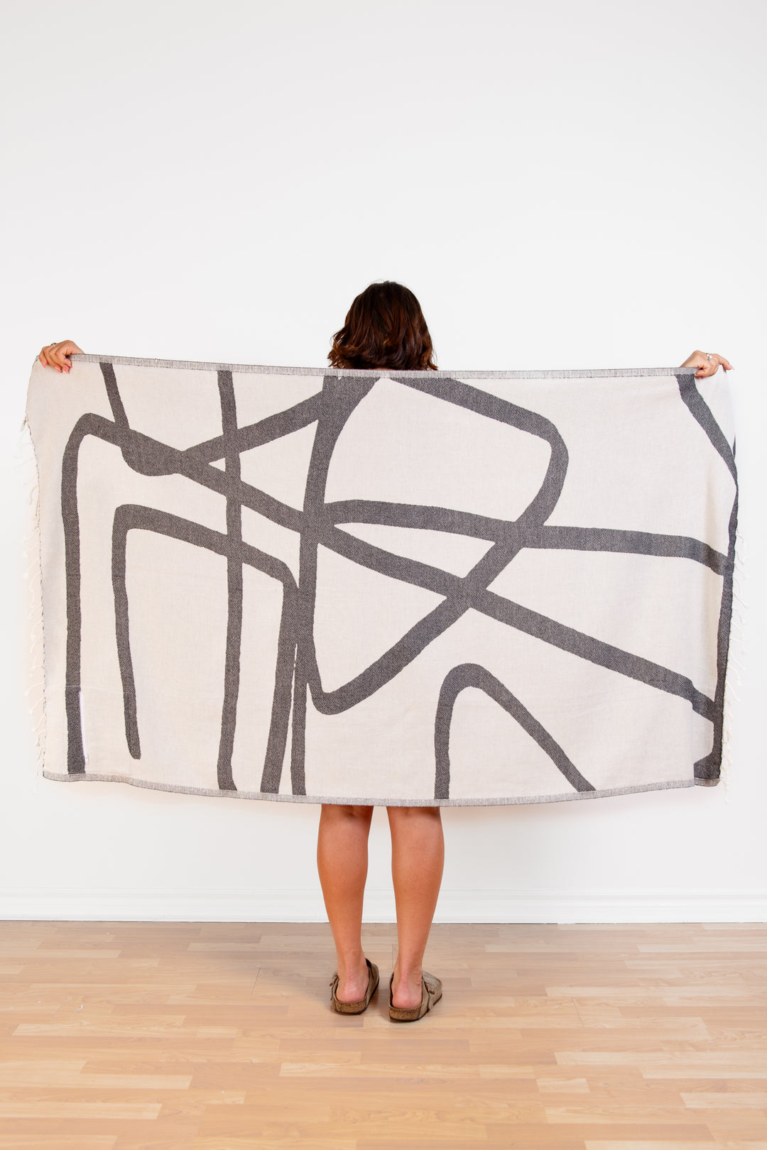 model holding up a Turkish cotton towel with an abstract white and dark grey design and eyelash fringe and on a white background #colour_granite