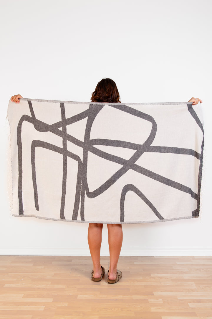 model holding up a Turkish cotton towel with an abstract white and dark grey design and eyelash fringe and on a white background #colour_granite