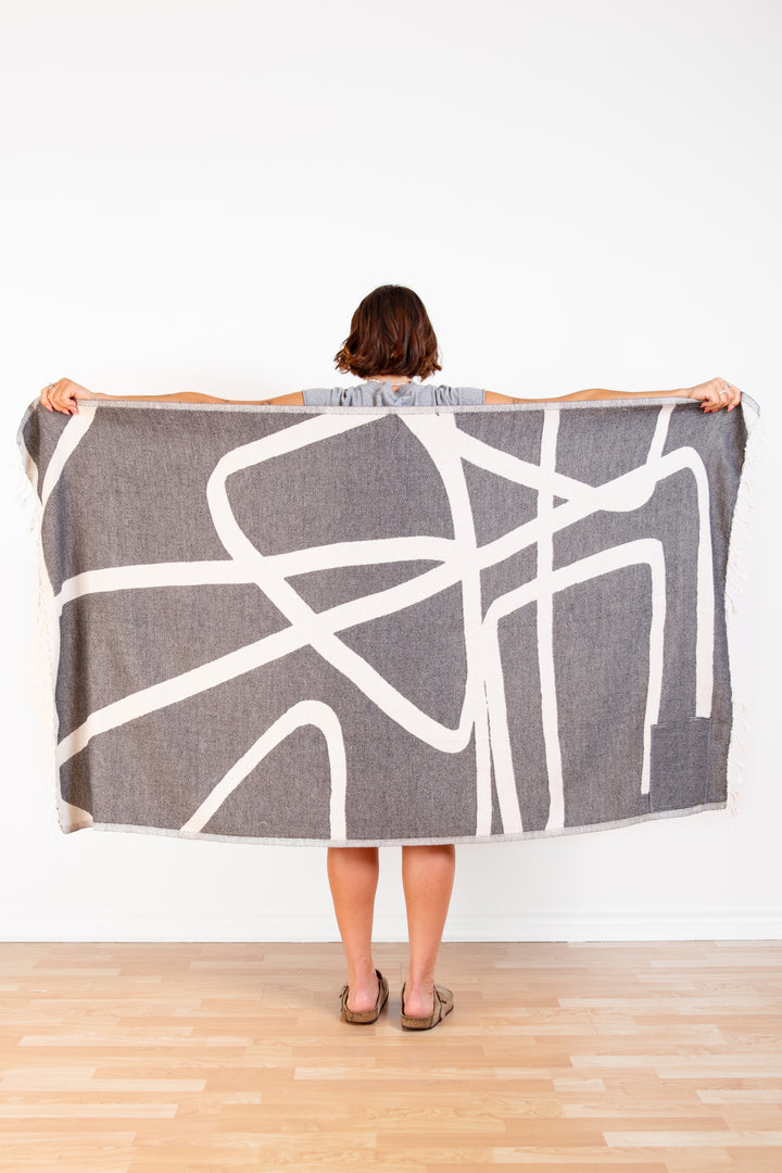 model holding up a Turkish cotton towel with an abstract white and dark grey design and eyelash fringe and on a white background #colour_granite