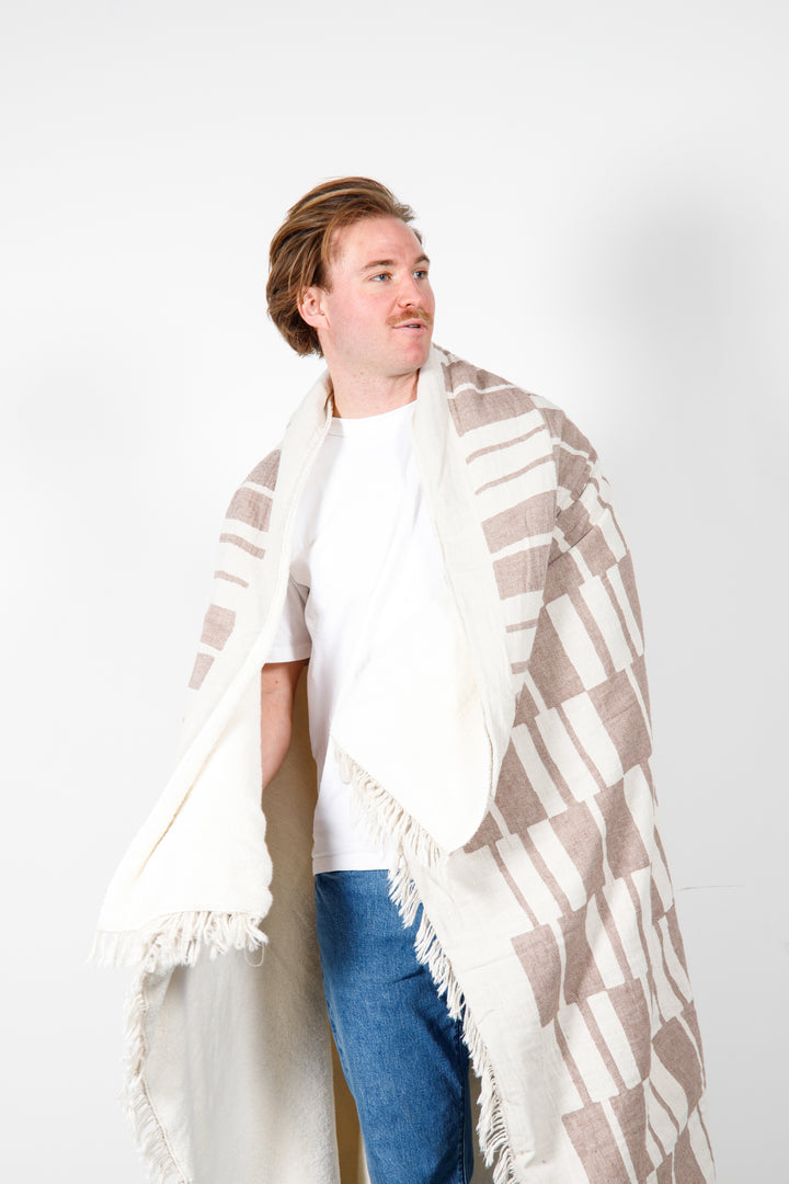 man wrapped in an off white and light brown fleece lined throw with modern checker board pattern and eyelash fringe  #colour_walnut