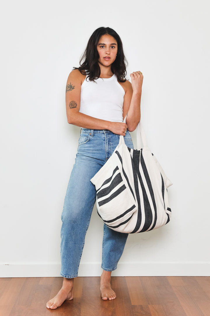 model in white tank top and blue jeans wearing oversized white and black striped Turkish cotton tote bag on a white background #colour_black