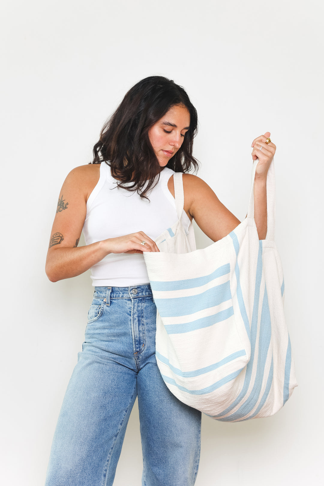 model in white tank top and blue jeans wearing oversized white and light blue striped Turkish cotton tote bag on a white background #colour_blue