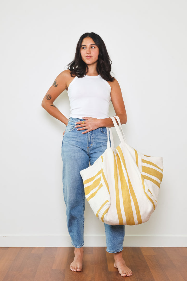 model in white tank top and blue jeans wearing oversized white and golden yellow striped Turkish cotton tote bag on a white background #colour_gold
