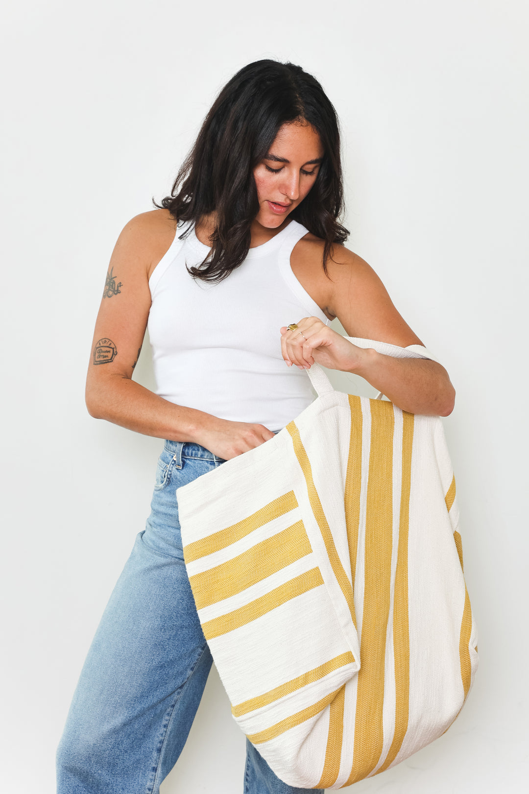 model in white tank top and blue jeans wearing oversized white and golden yellow striped Turkish cotton tote bag on a white background #colour_gold