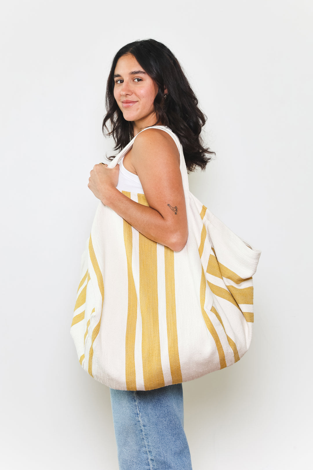 model in white tank top and blue jeans wearing oversized white and golden yellow striped Turkish cotton tote bag on a white background #colour_gold