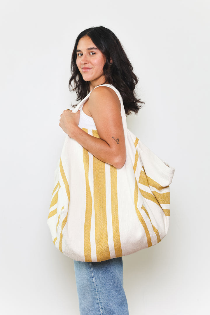 model in white tank top and blue jeans wearing oversized white and golden yellow striped Turkish cotton tote bag on a white background #colour_gold